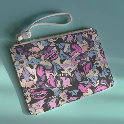 Rectangular wristlet clutch featuring a dark background with colorful bats, skulls, eyeballs, and vampire mouths. White strap and gold zipper visible.